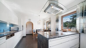 Une cuisine moderne dotée d’un grand îlot central, de meubles blancs et offrant une vue sur l’extérieur.