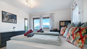 Une chambre avec deux lits, une grande fenêtre avec des rideaux, un tableau au mur et une table de chevet avec une lampe.