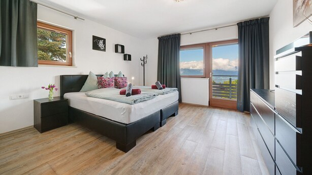 Une chambre à coucher avec un lit, une table de chevet, une commode, une fenêtre avec des rideaux et une vue sur le ciel.