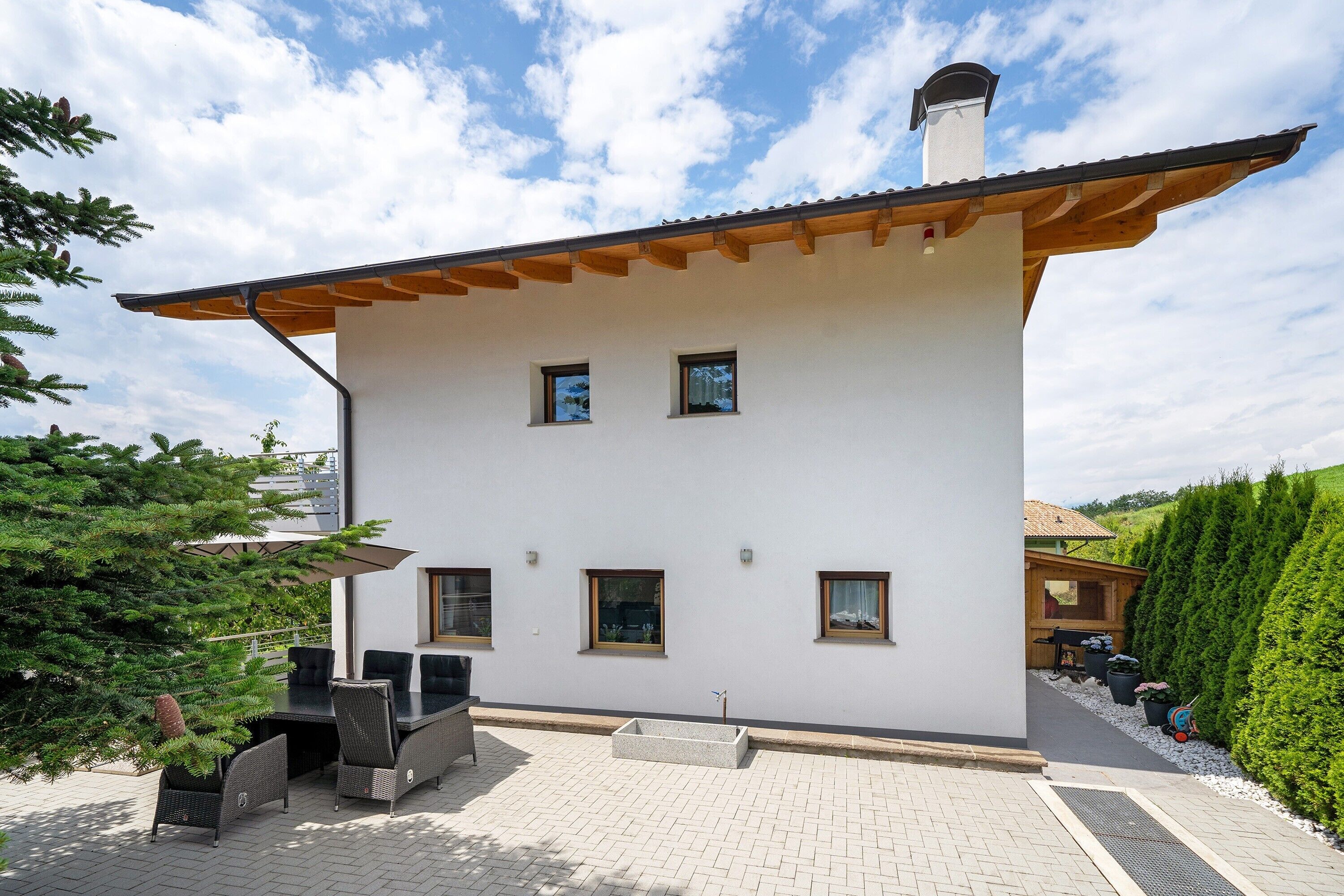 Ein modernes, zweistöckiges Haus mit Terrasse, Sitzgelegenheiten im Freien und einem gepflegten Garten.