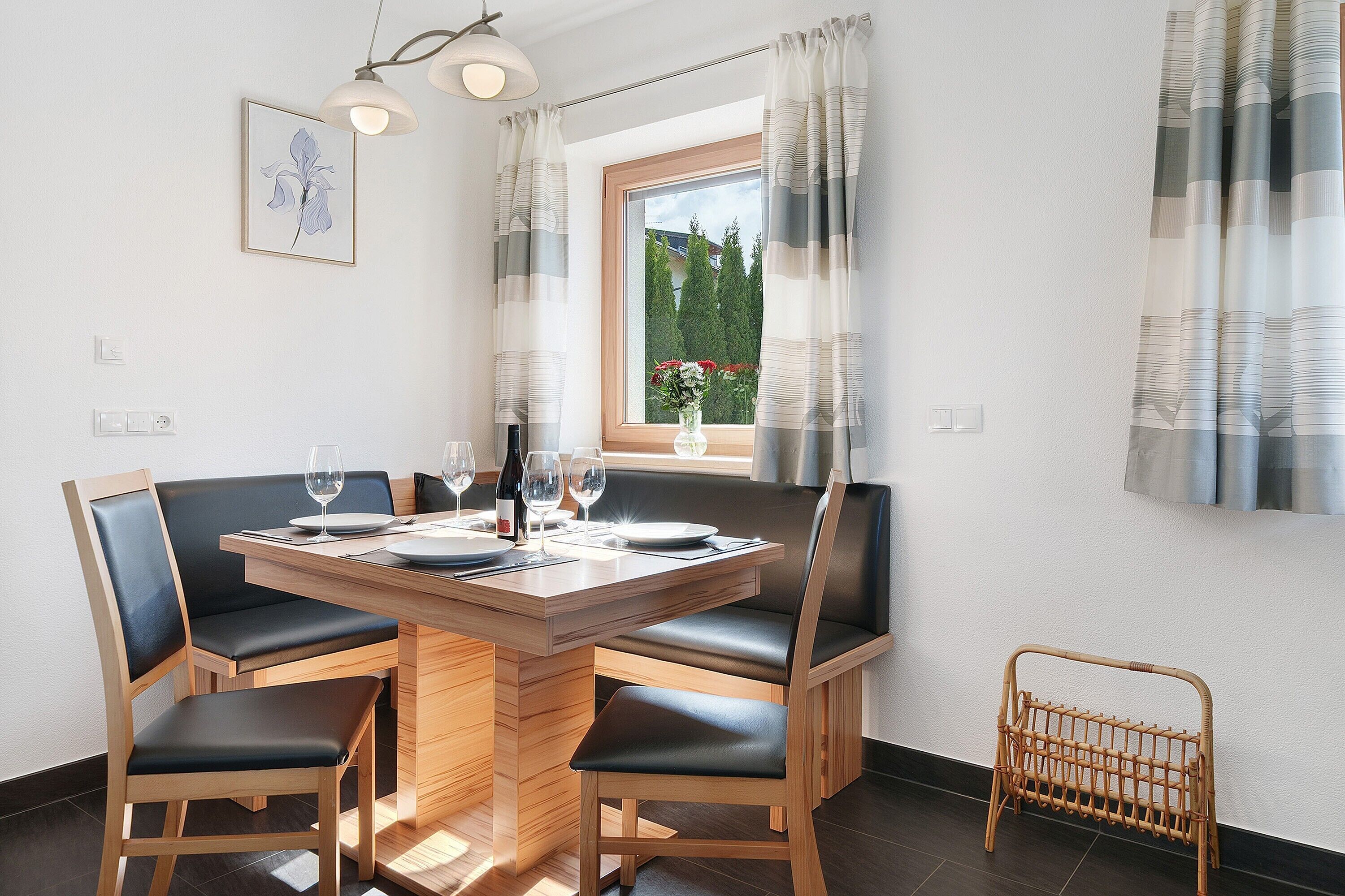 Un comedor con una mesa de madera, cuatro sillas y un ventanal con cortinas.