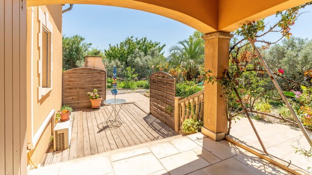 Un patio cubierto con piso de madera, una mesa pequeña y plantas en macetas.