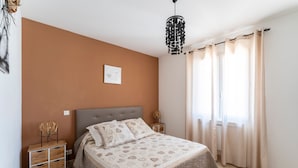 Un dormitorio con cama, mesitas de noche, una lámpara colgante y un ventanal con cortinas.