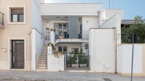 Edificio residencial de dos pisos con balcón, escaleras y entrada protegida por una reja.