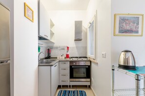 Uma cozinha compacta com forno embutido, fogão a gás e chaleira em um suporte.