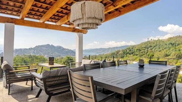 An outdoor patio with a wooden table and chairs, a hanging light fixture, and a scenic view of hills and a lake. - LUXO Casa Valle de Bravo con jacuzzi y espectacular Vista al Lago (Valle de Bravo)