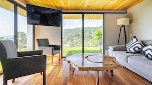 A modern living room with a wooden ceiling, large windows, a flat-screen TV, a sofa, a coffee table, and a floor lamp. - LUXO Casa Valle de Bravo con jacuzzi y espectacular Vista al Lago (Valle de Bravo)