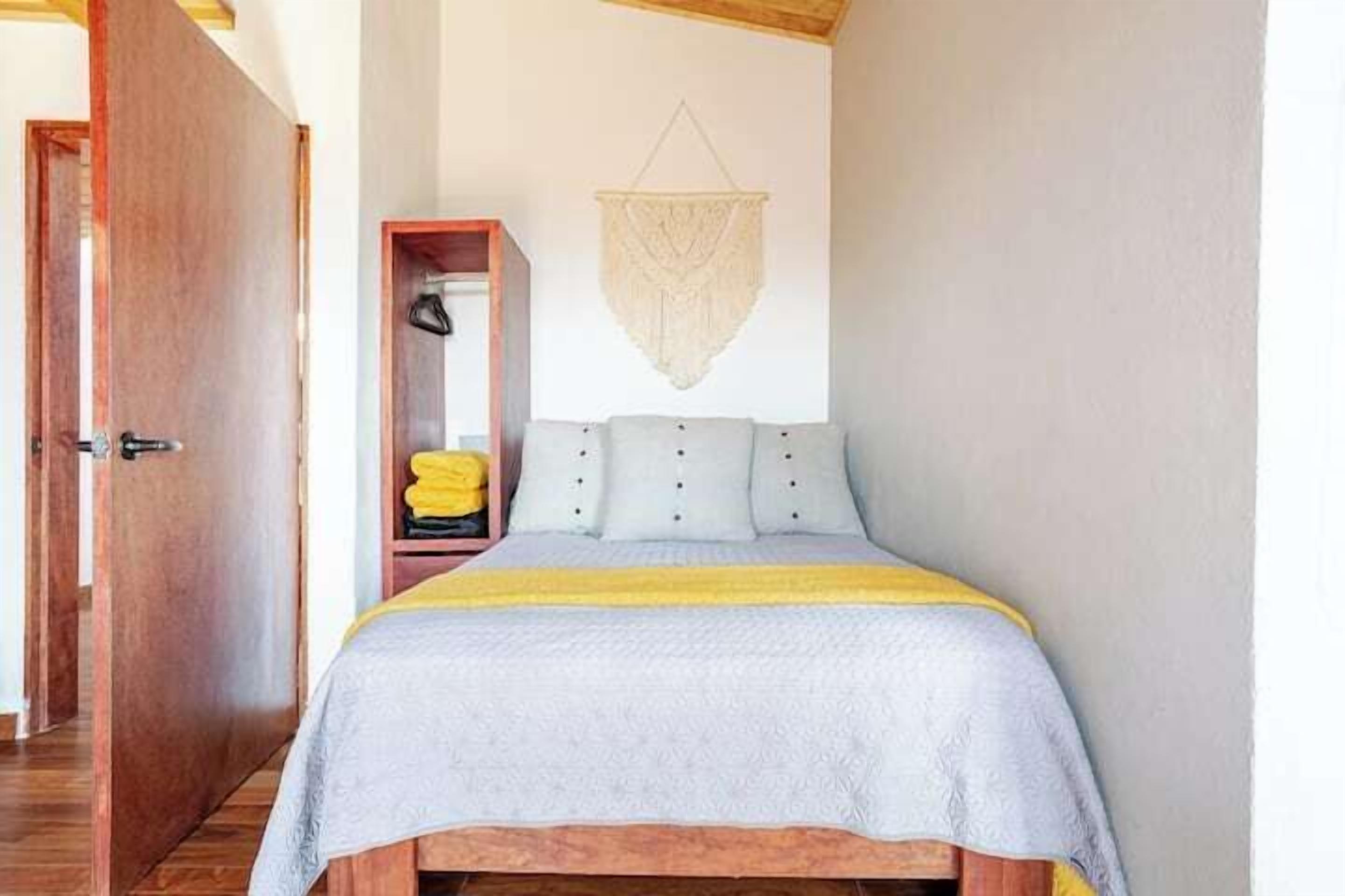 Ein Schlafzimmer mit einem Bett, einem hölzernen Kopfteil, einer hängenden Makramee-Dekoration und einem Kleiderschrank mit gefalteter Kleidung.