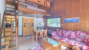 A cozy cabin interior with a loft bed, wooden furniture, a dining area, and a large window with a view. - Apartment rental near the slopes in the Rochebrune area (Megève)