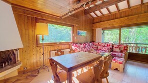 A wooden cabin interior with a dining table, chairs, a sofa, and a large window. - 1 Douny Apartment rental near the slopes Rochebrune area (Megève)