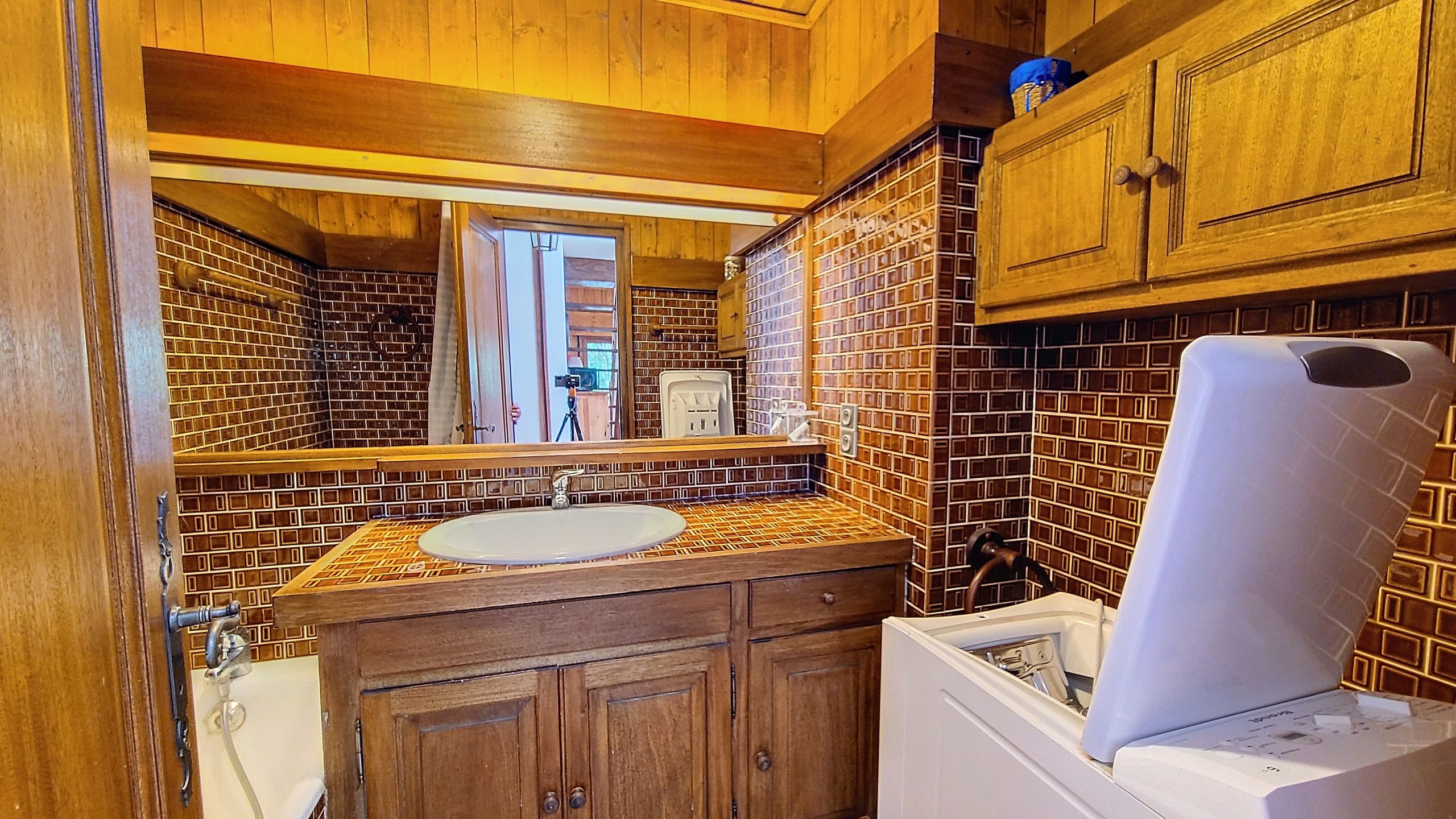 A bathroom with a wooden vanity, a sink, and a white washing machine.