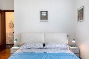 Quarto com uma cama, duas mesas de cabeceira, uma luminária na parede e um quadro emoldurado.