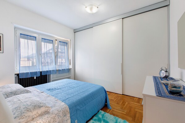 Un dormitorio con cama, cómoda, ventana con cortinas y armario.