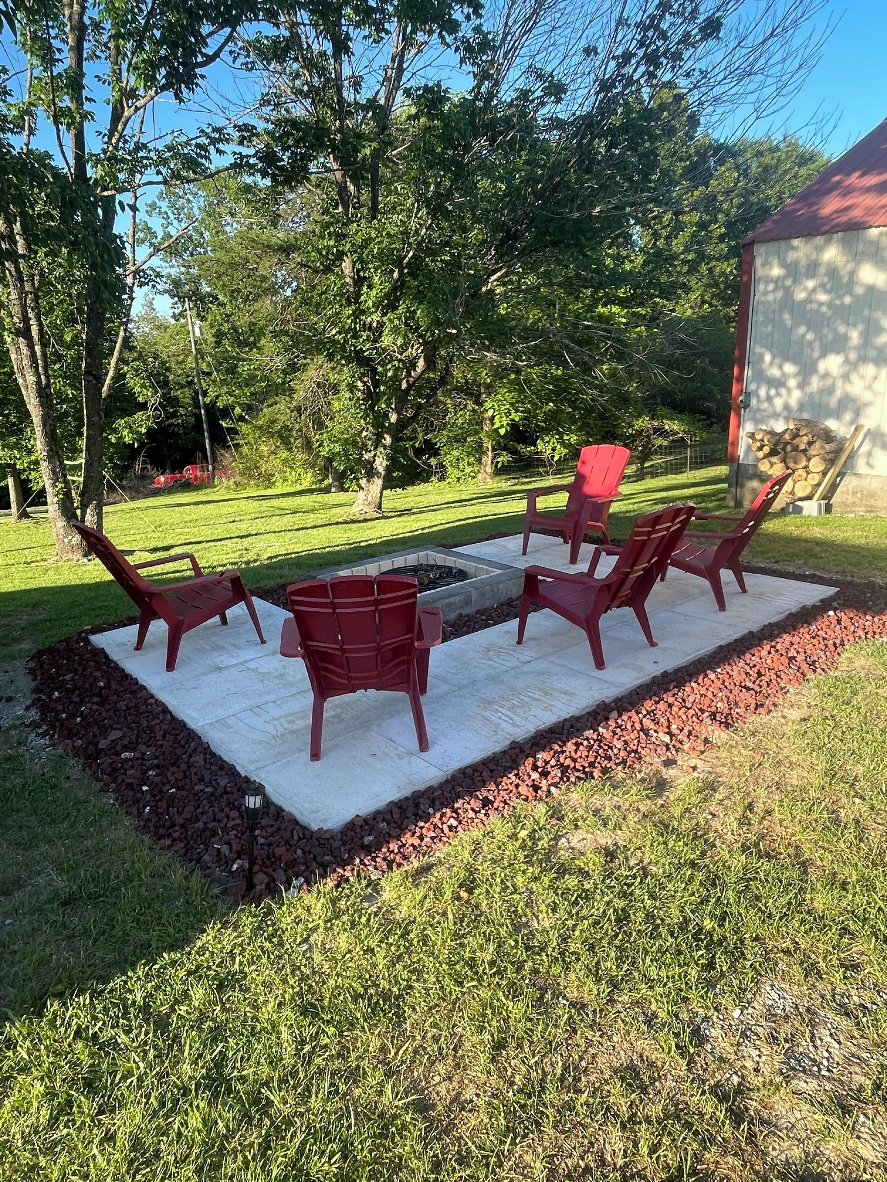 A patio area with a fire pit and four red chairs arranged around it.