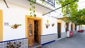 Entrada de un edificio con puerta de madera, plantas en macetas y suelo de baldosas.