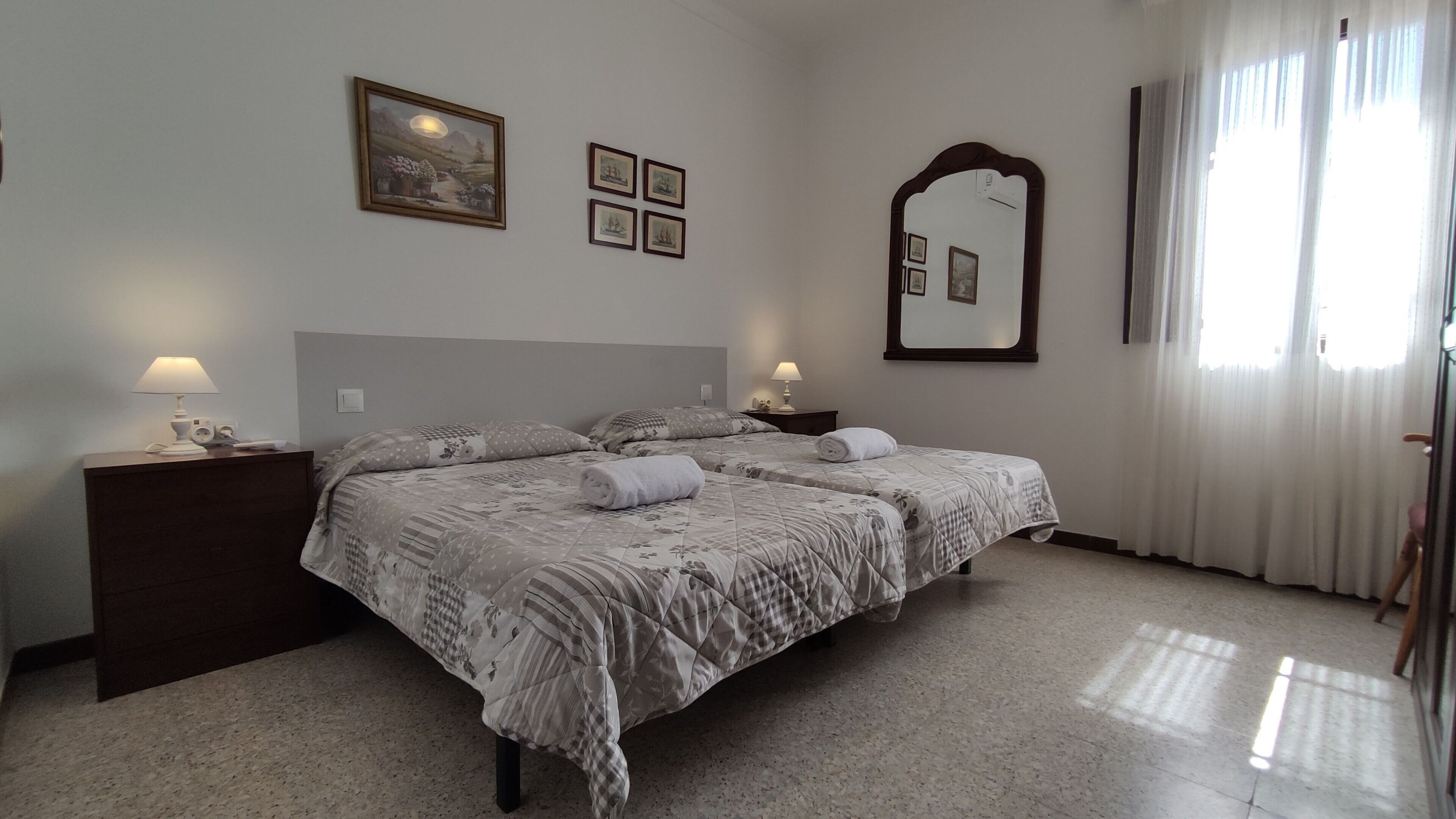 A bedroom with a bed, two bedside tables, a nightstand, a mirror, and a window with curtains.