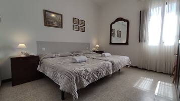 A bedroom with a bed, two bedside tables, a nightstand, a mirror, and a window with curtains.