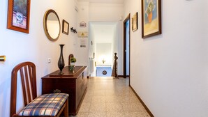 Un pasillo con una silla de madera, un espejo y un florero sobre una mesa.