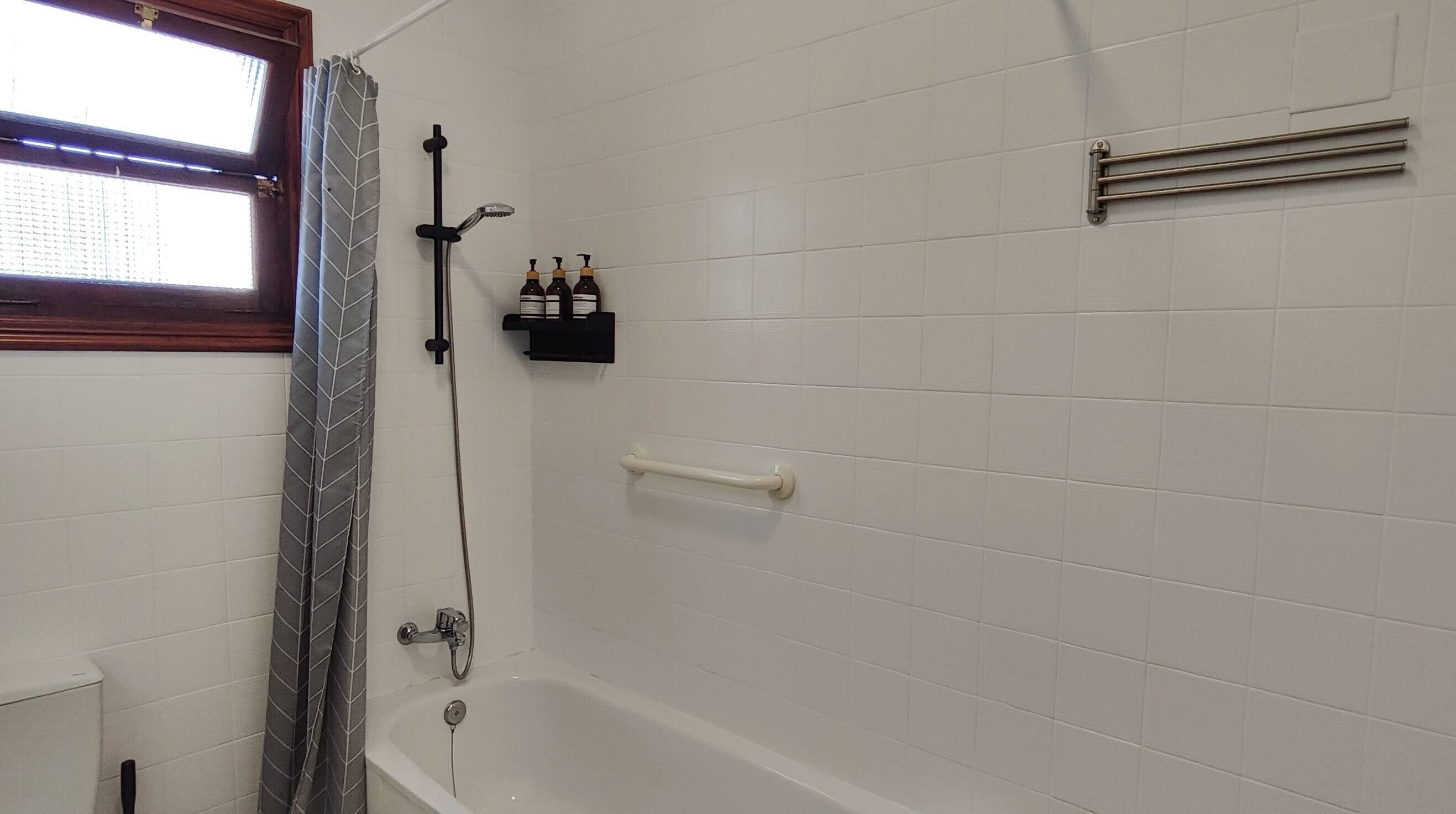 Een badkamer met een douche, toilet, badkuip, handdoekrek en een plank met toiletartikelen.