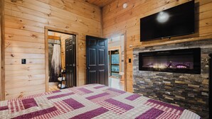 Un dormitorio de cabaña de madera con colcha acolchada, chimenea de piedra y televisor montado.
