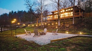 Una cabaña con terraza y zona de estar al aire libre, rodeada de árboles y un sendero de grava.