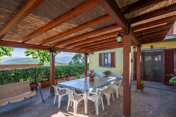 Une terrasse couverte avec une table et des chaises, des plantes en pot et une vue sur les montagnes.