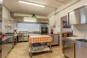 Una cocina industrial con electrodomésticos de acero inoxidable, piso de baldosas y un carrito con contenedores de almacenamiento.