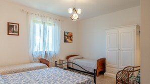 A bedroom with two single beds, a wooden nightstand, a chair, a wardrobe, and a chandelier. - Holiday Home 'Podere Calistri' with Mountain View, Wi-Fi and Air Conditioning (Larciano)