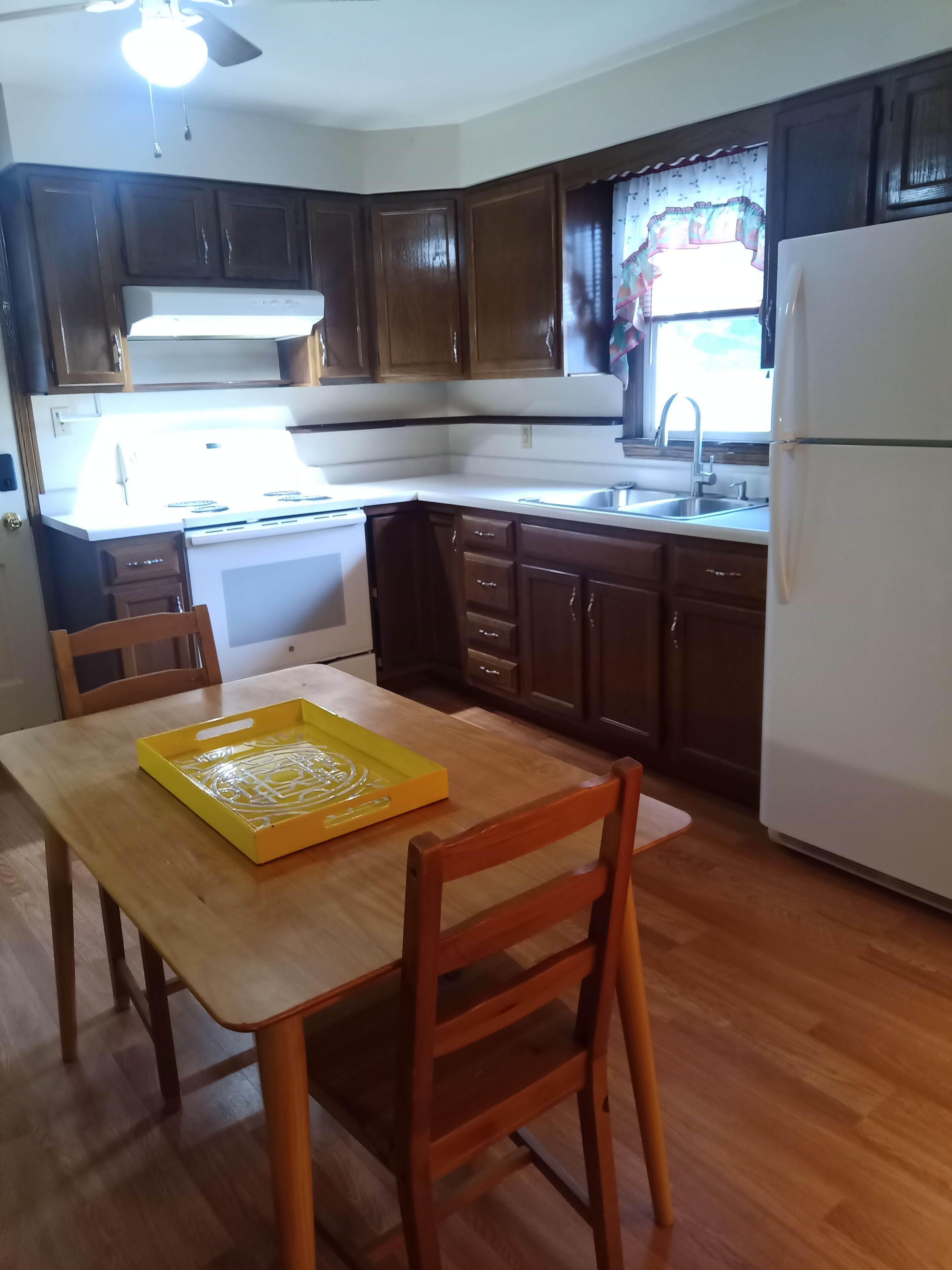 A compact kitchen with dark wooden cabinets, a white refrigerator, and a wooden dining table with chairs.