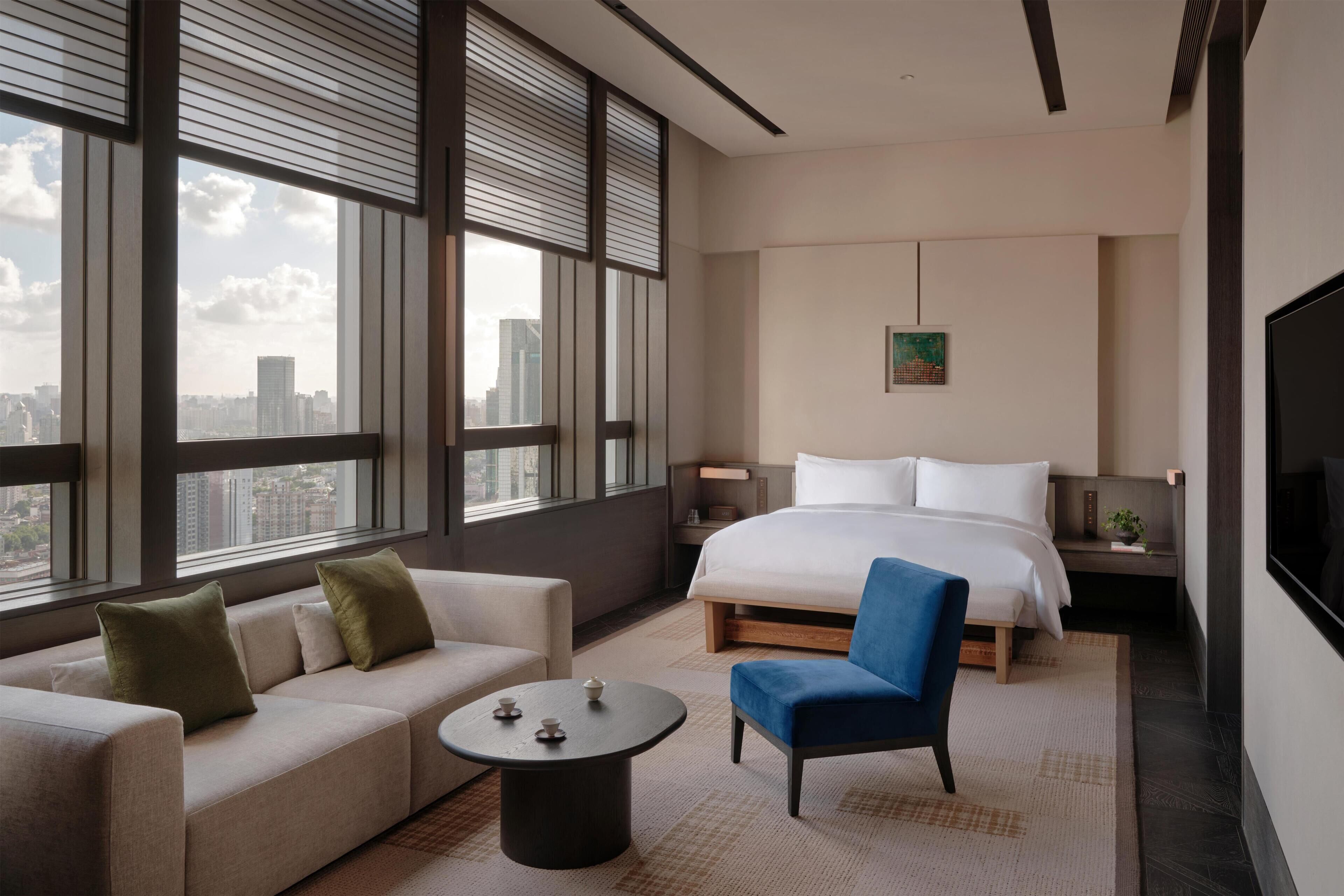 Ein modernes Hotelzimmer mit einem großen Bett, einer Couch, einem Sessel, einem kleinen Tisch und einem Fernseher.
