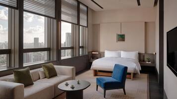 Ein modernes Hotelzimmer mit einem großen Bett, einer Couch, einem Sessel, einem kleinen Tisch und einem Fernseher.