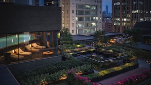 Une terrasse sur le toit dotée d’un salon fermé par des baies vitrées, d’un espace extérieur aménagé pour s’asseoir et d’un jardin avec des plantes et des fleurs.