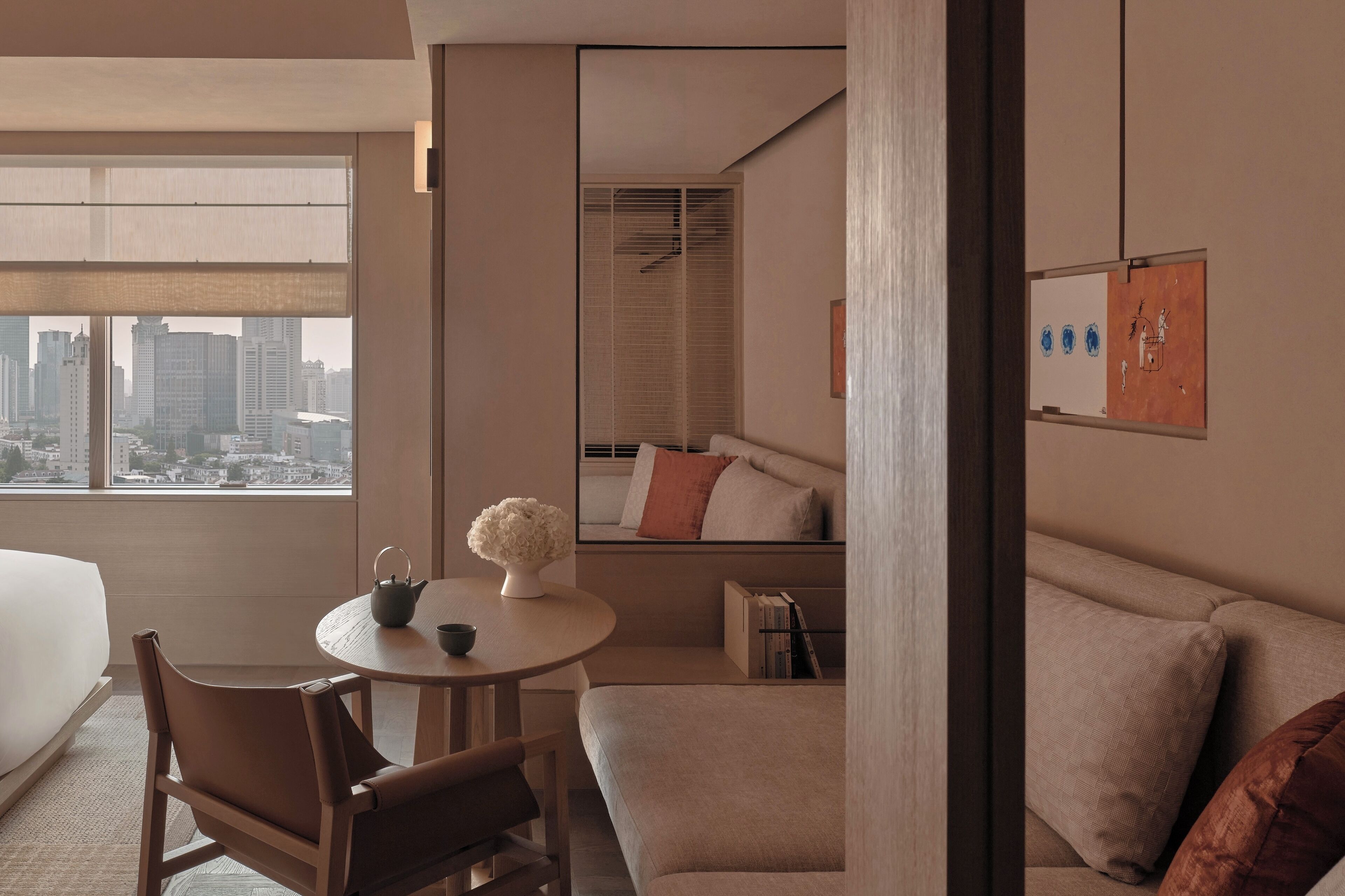 Una habitación de hotel moderna con un ventanal grande, una mesa redonda con un florero, un sofá y una cama.