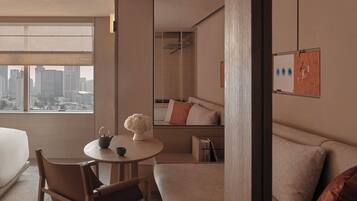 Una habitación de hotel moderna con un ventanal grande, una mesa redonda con un florero, un sofá y una cama.