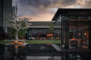 A modern building with a reflective pool, a unique tree sculpture, and a dining area visible through glass walls. - Alila Shanghai (Shanghai)