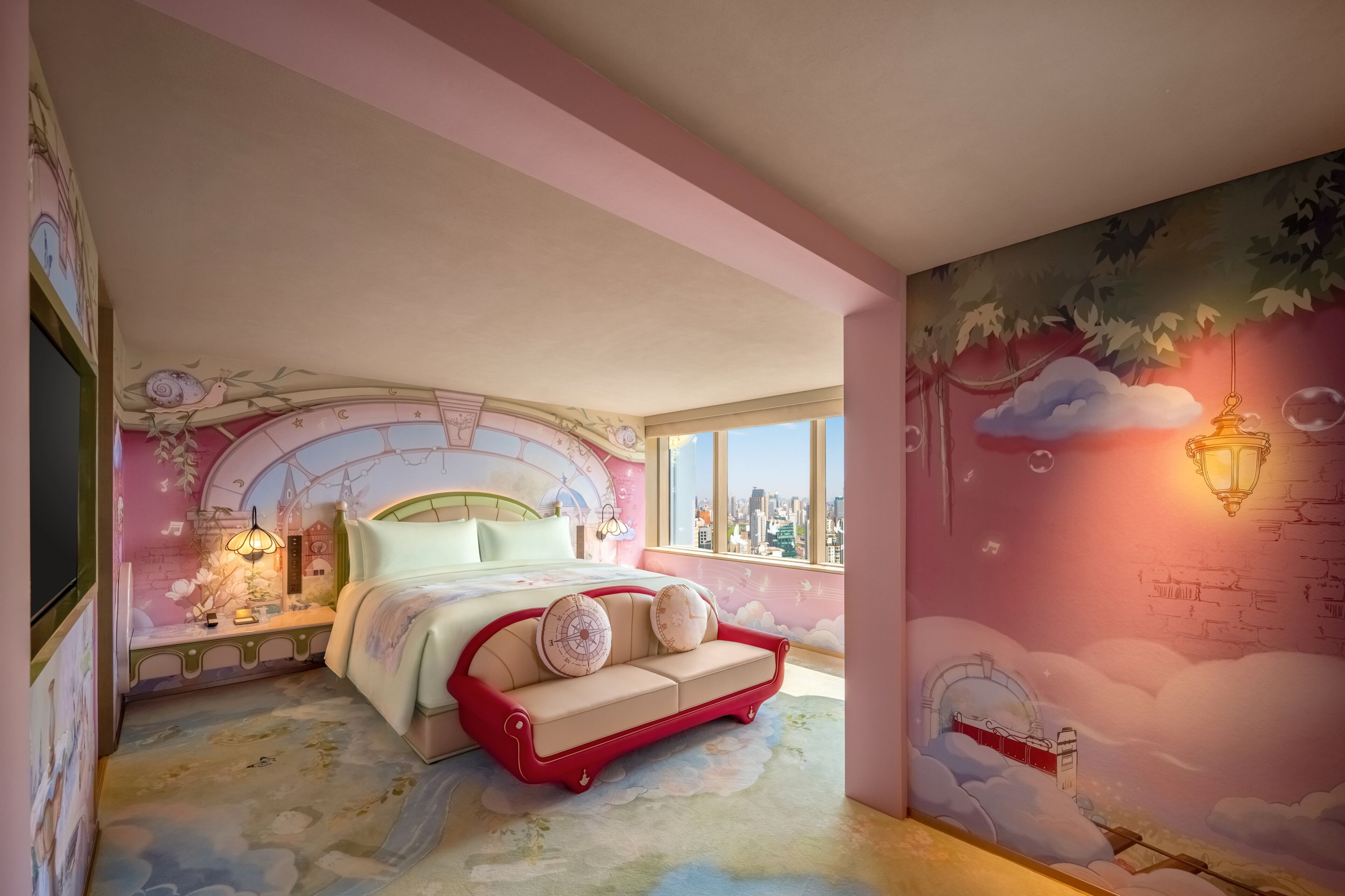 Un dormitorio con cama, un sofá rojo, una mesita de noche, una lámpara y vistas a la ciudad.