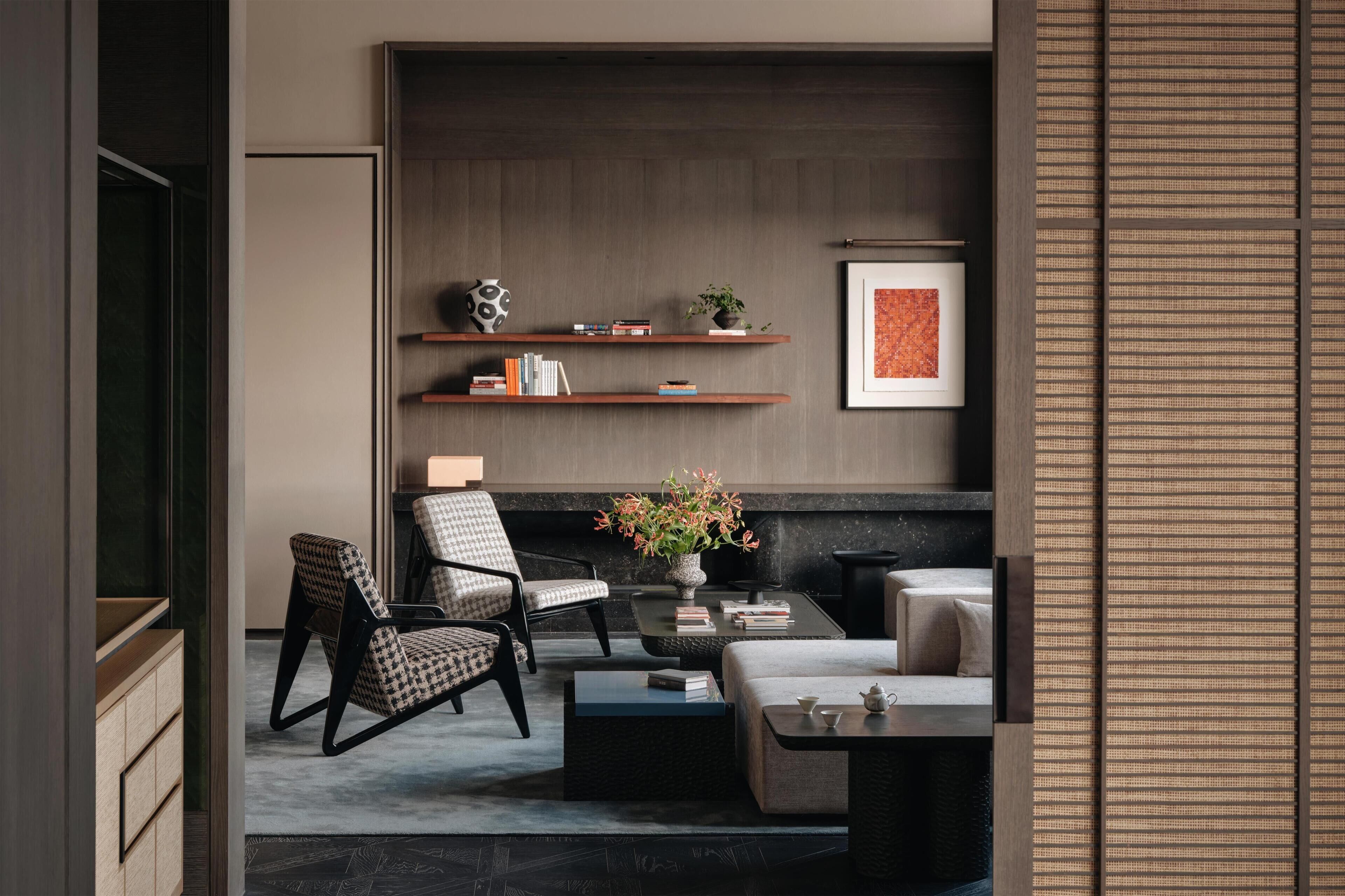Una sala de estar moderna con sofá, sillón, mesa de centro y estanterías con libros y objetos decorativos.