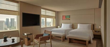 Ein Hotelzimmer mit zwei Betten, einem Fernseher, einem kleinen Tisch mit Stuhl und Blick auf die Stadt.