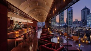Un bar avec vue sur la ville, des sièges rouges et un barman.