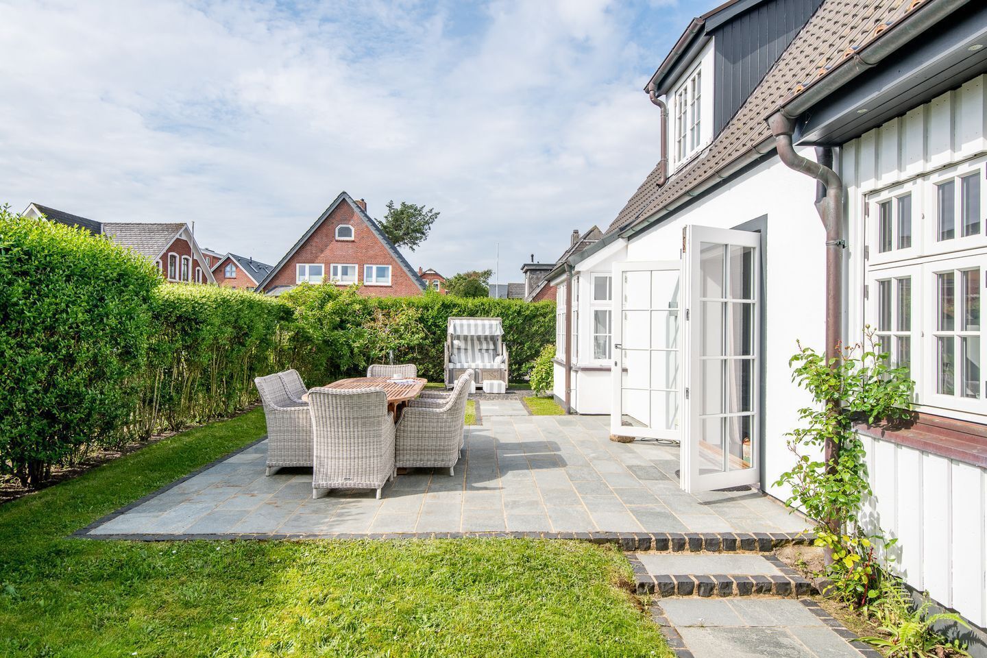 A patio area with outdoor furniture, a white door, and a hedge.