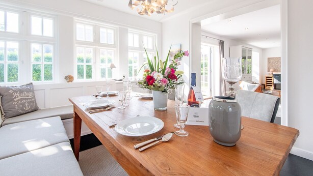 Un coin repas avec une table en bois dressée pour quatre personnes, un vase rempli de fleurs et une bouteille de vin.