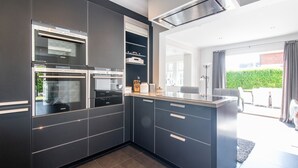 Une cuisine moderne avec des meubles de couleur sombre, des fours encastrés et une grande fenêtre donnant sur un jardin.