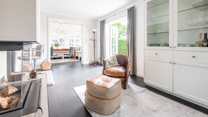 Un salon spacieux agrémenté d’une cheminée moderne, d’un fauteuil en cuir et d’une vitrine contenant des objets décoratifs.
