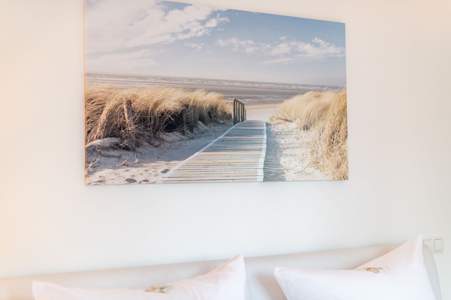 Une scène de plage avec une promenade en bois menant à l’océan, le tout encadré et accroché au mur.