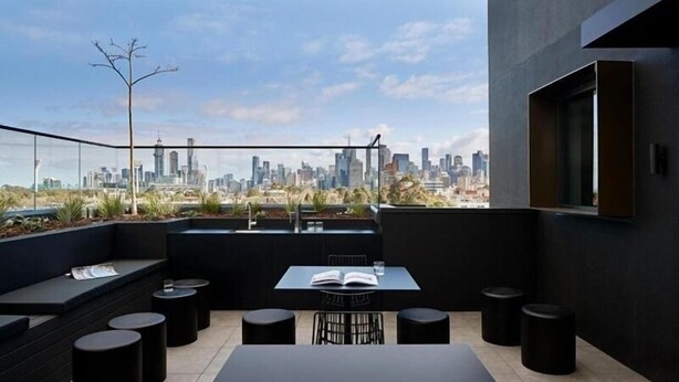 Una terraza en la azotea con vistas a un horizonte urbano, una mesa con un libro y asientos negros.