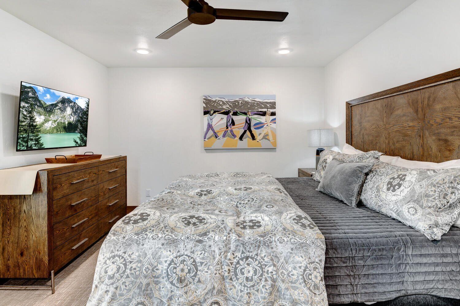 Un dormitorio con cama, cómoda, ventilador de techo, televisión y dos cuadros en la pared.