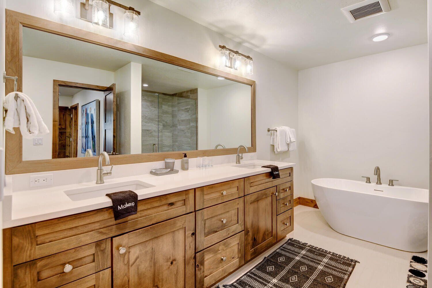 A modern bathroom with a double vanity, a large mirror, and a freestanding bathtub.