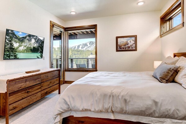 Un dormitorio con cama, cómoda de madera, televisión y ventana con vistas a una montaña y un lago.