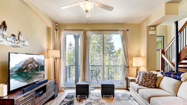 A living room with a television, sofa, and a view of a balcony with a wooden deck.