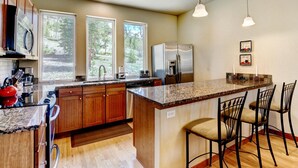 A modern kitchen with wooden cabinets, granite countertops, a stainless steel refrigerator, and a large island with bar stools.